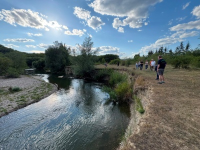 Flussufer mit Wandergruppe im Burgenland, Österreich, bei Sonnenschein und Wolken.