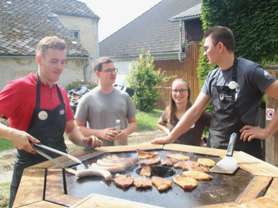 Helfer an der Feuertonne beim Grillen von Brot, Kotelette und Grillw&uuml;rsten
