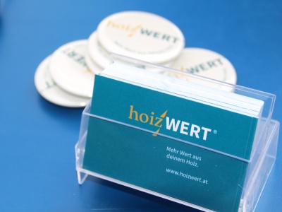 Detailaufnahme von hoizWERT Visitkarten in Plexist&auml;nder und Flaschen&ouml;ffner mit hoizWERT Logo unscharf im Hintergrund