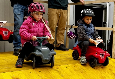 zwei Kinder sitzen auf einem Bobby Car und fahren eine Startrampe hinunter