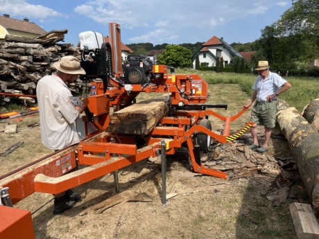 Mobiles S&auml;gewerk im Einsatz beim Kunden dahinter Holzpolter. Waldbesitzer entscheidet vor Ort &uuml;ber den idealen Einschnitt der Baumst&auml;mme.